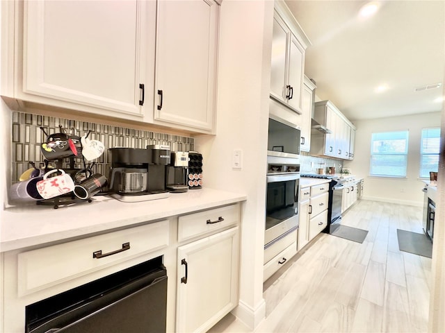 kitchen with electric range, oven, light countertops, white cabinetry, and backsplash