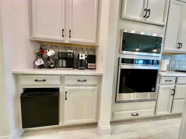 kitchen with tasteful backsplash, white cabinetry, stainless steel appliances, and light countertops