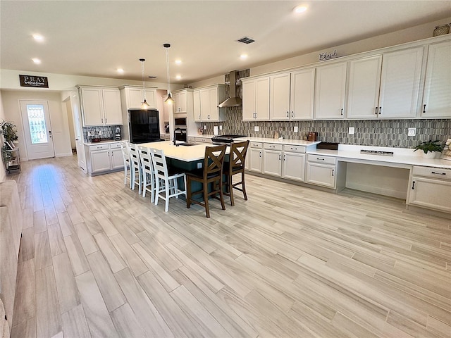 kitchen with visible vents, stainless steel oven, a kitchen breakfast bar, wall chimney exhaust hood, and tasteful backsplash