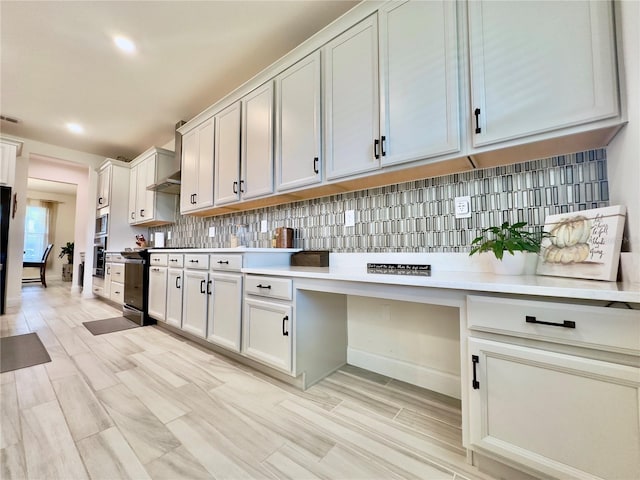 kitchen with black / electric stove, visible vents, light countertops, wall chimney range hood, and backsplash