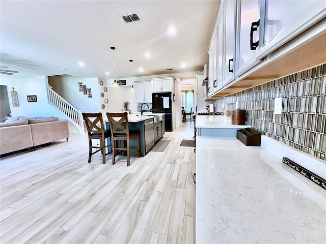 kitchen with visible vents, a kitchen breakfast bar, open floor plan, light countertops, and dishwasher