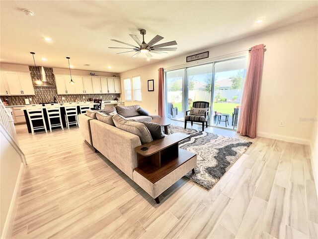 living area with a ceiling fan, light wood-style floors, baseboards, and a wealth of natural light