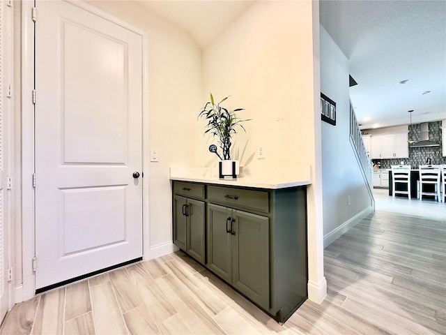 bar featuring light wood finished floors, backsplash, baseboards, and wall chimney range hood