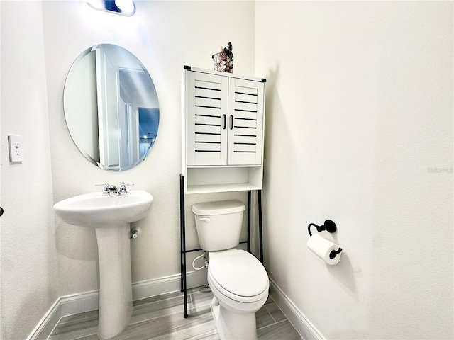 bathroom featuring toilet, wood finished floors, baseboards, and a sink