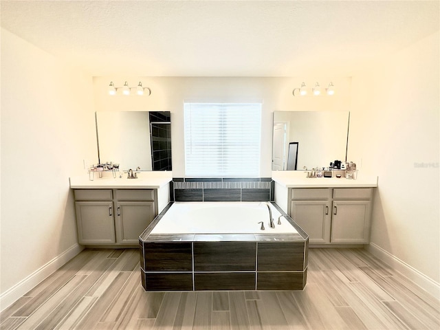 bathroom featuring two vanities, a bath, baseboards, and wood finish floors