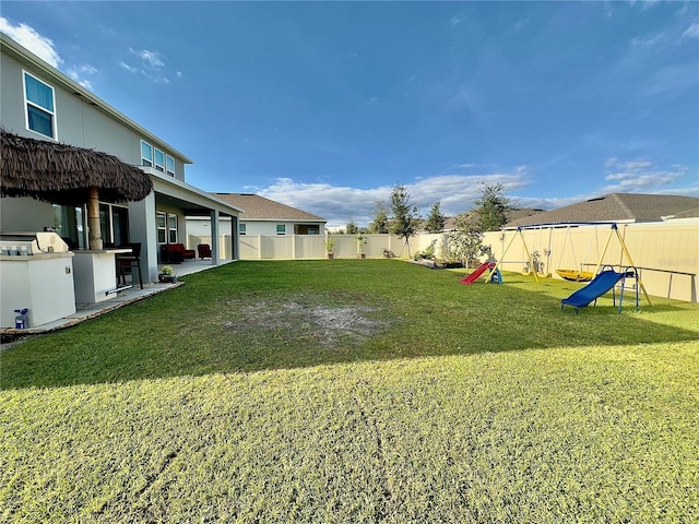 view of yard featuring exterior kitchen, a playground, a fenced backyard, and a patio area