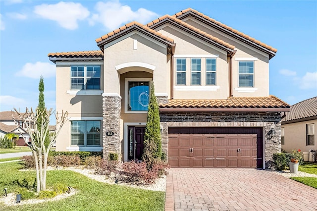 mediterranean / spanish home featuring stone siding, decorative driveway, an attached garage, and stucco siding