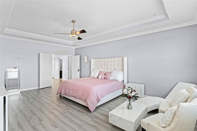 bedroom featuring crown molding, a raised ceiling, ceiling fan, light wood-type flooring, and baseboards