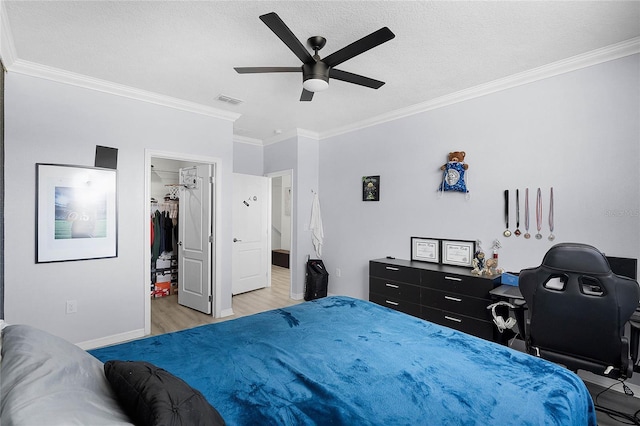 bedroom featuring a textured ceiling, wood finished floors, visible vents, ornamental molding, and a walk in closet