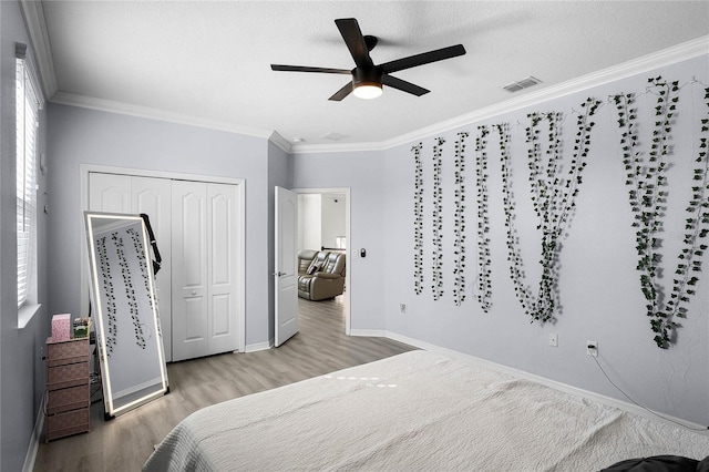 bedroom with wood finished floors, visible vents, baseboards, a closet, and crown molding