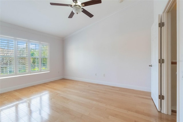 spare room featuring vaulted ceiling, ornamental molding, light wood-type flooring, and baseboards