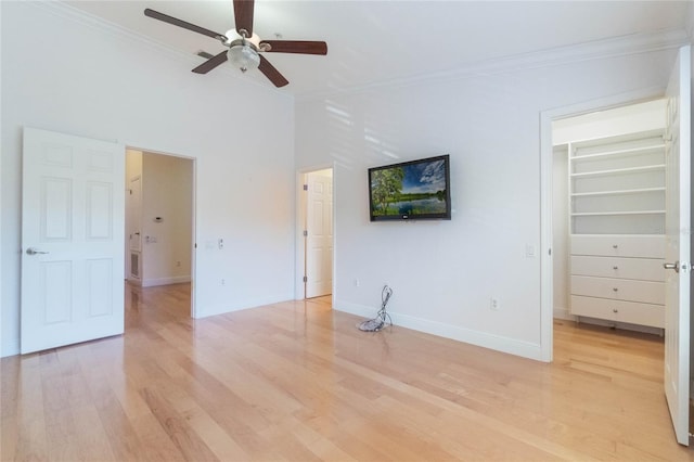 unfurnished bedroom with a closet, light wood-style flooring, a spacious closet, ornamental molding, and baseboards