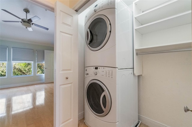 clothes washing area featuring light wood-type flooring, stacked washer / drying machine, laundry area, and baseboards