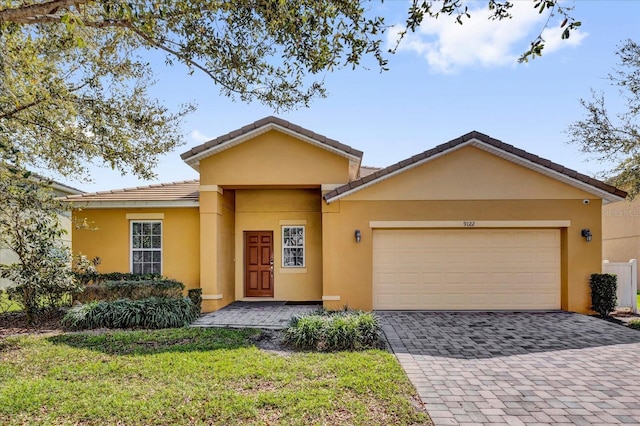 ranch-style house with an attached garage, a tile roof, decorative driveway, and stucco siding