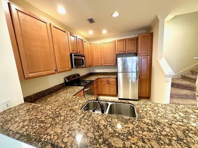 kitchen with stainless steel appliances, visible vents, a sink, and dark stone countertops