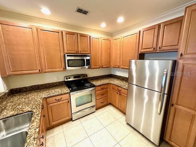 kitchen featuring stainless steel appliances, visible vents, brown cabinetry, light tile patterned flooring, and a sink