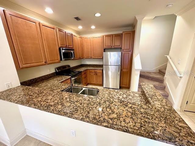 kitchen with stainless steel appliances, recessed lighting, brown cabinetry, dark stone countertops, and a peninsula