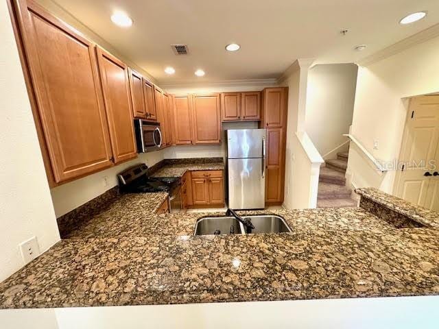 kitchen with visible vents, ornamental molding, dark stone countertops, stainless steel appliances, and a sink