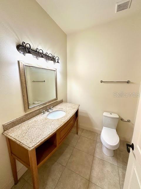 bathroom featuring baseboards, visible vents, toilet, tile patterned floors, and vanity