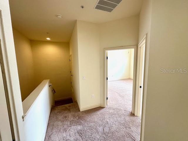 hall featuring carpet, visible vents, baseboards, and an upstairs landing