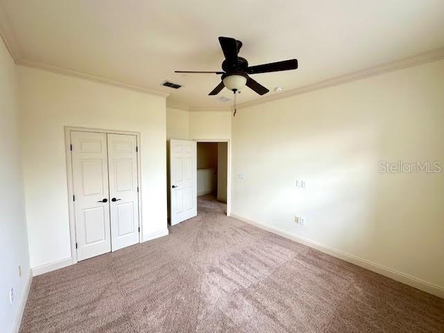 unfurnished bedroom featuring carpet floors, baseboards, visible vents, and crown molding