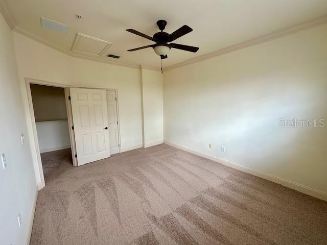 unfurnished bedroom with carpet floors, ornamental molding, attic access, and baseboards