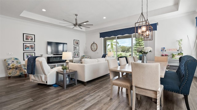 dining area with ornamental molding, a tray ceiling, ceiling fan with notable chandelier, and wood finished floors