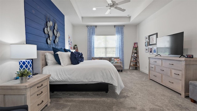 bedroom with light colored carpet, wood walls, a ceiling fan, baseboards, and a raised ceiling