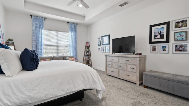 bedroom with light carpet, a ceiling fan, visible vents, baseboards, and a raised ceiling