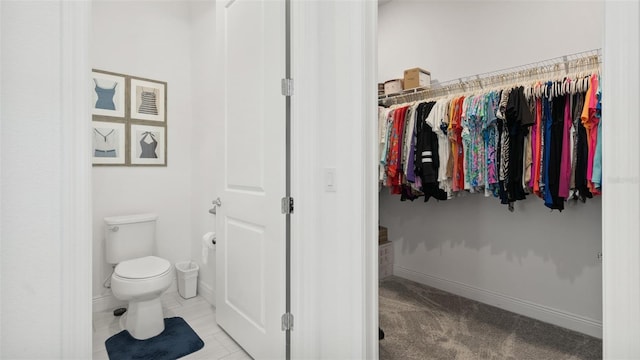 bathroom featuring a walk in closet, toilet, and baseboards