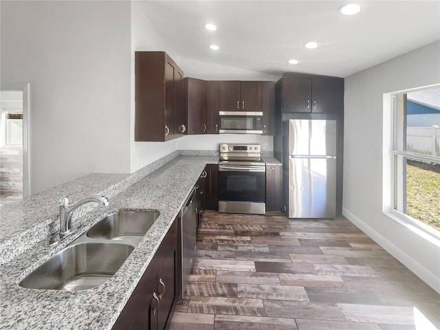 kitchen with light stone counters, dark brown cabinetry, stainless steel appliances, dark wood-style flooring, and a sink