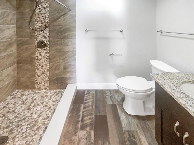 bathroom featuring toilet, wood finished floors, vanity, baseboards, and a tile shower