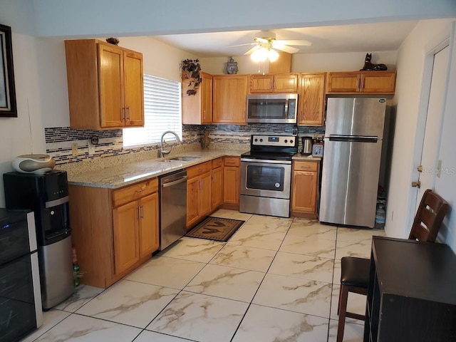 kitchen with tasteful backsplash, appliances with stainless steel finishes, light stone counters, marble finish floor, and a sink