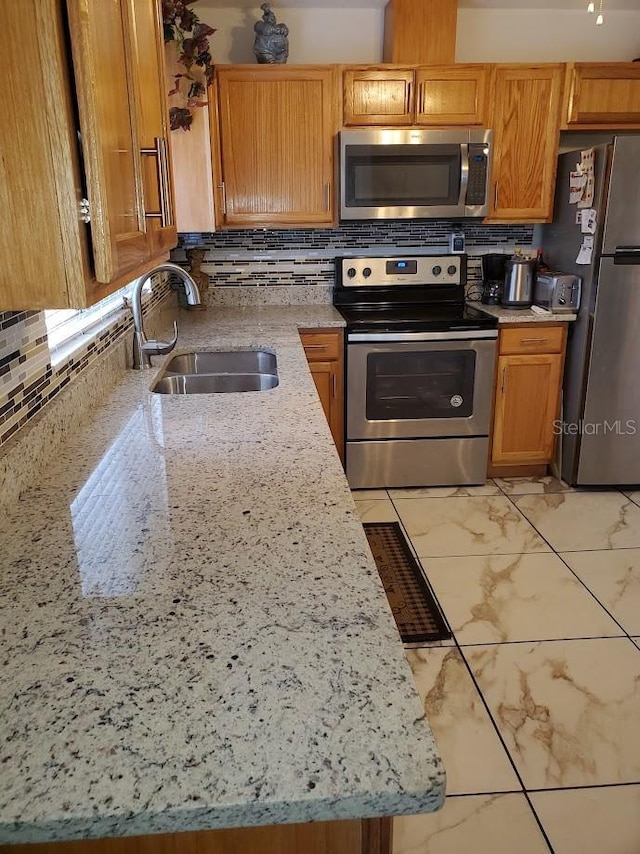 kitchen featuring stainless steel appliances, marble finish floor, a sink, and tasteful backsplash