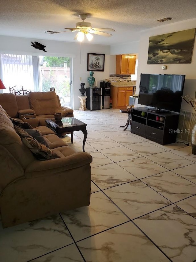 living area featuring a textured ceiling, marble finish floor, visible vents, and a ceiling fan