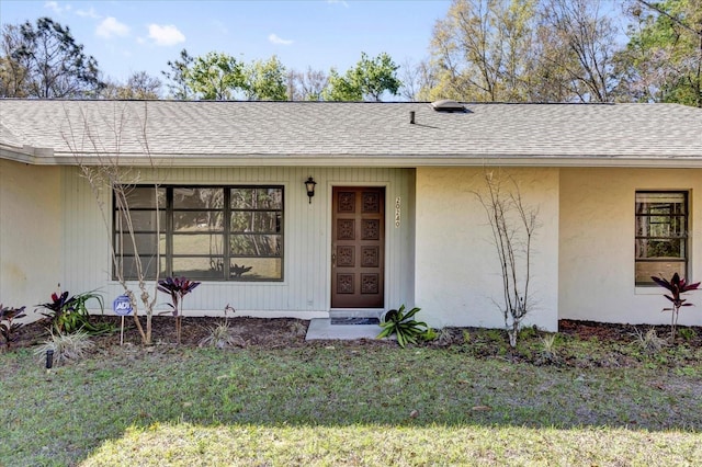 entrance to property featuring a shingled roof, a yard, and stucco siding