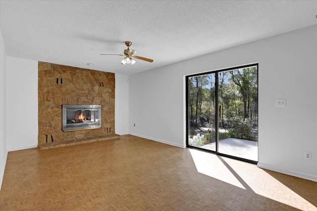 unfurnished living room with a textured ceiling, ceiling fan, a fireplace, and baseboards