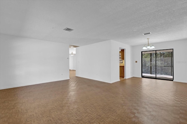 unfurnished room featuring a textured ceiling, baseboards, visible vents, and a notable chandelier