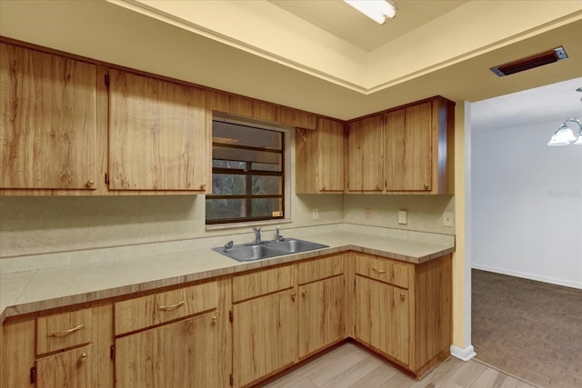 kitchen featuring light countertops, visible vents, light brown cabinets, a sink, and baseboards