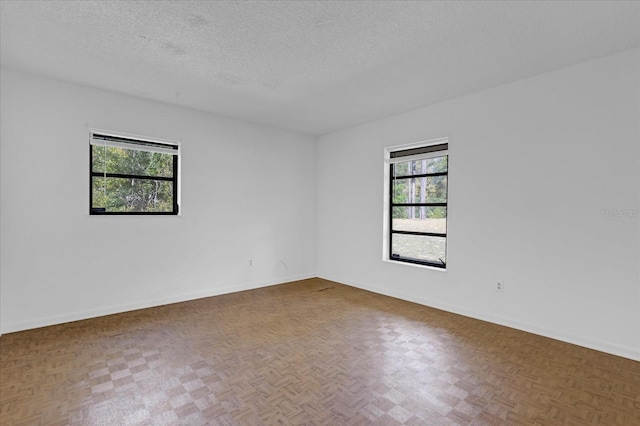 empty room featuring a textured ceiling, baseboards, and a wealth of natural light