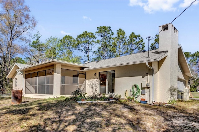 view of front facade with a sunroom, a chimney, an attached garage, and stucco siding