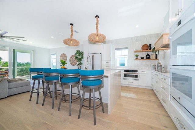 kitchen with open shelves, custom range hood, light wood-style floors, a kitchen island, and white appliances