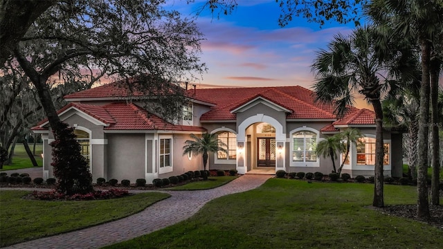 mediterranean / spanish-style home featuring driveway, a tiled roof, a front lawn, and stucco siding