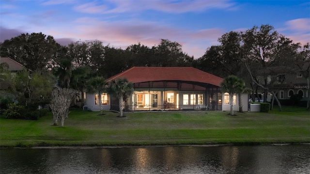 rear view of house with a water view, a yard, and a tiled roof