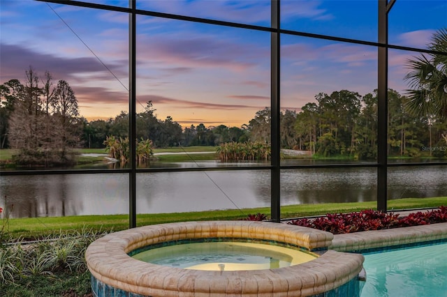 pool at dusk featuring an in ground hot tub and a water view