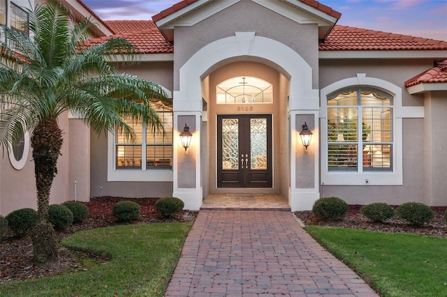 exterior entry at dusk with stucco siding, a tile roof, and french doors