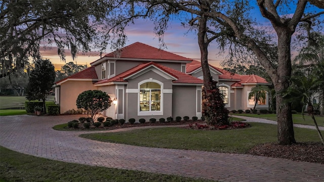 view of front of house with decorative driveway, a tile roof, a yard, and stucco siding