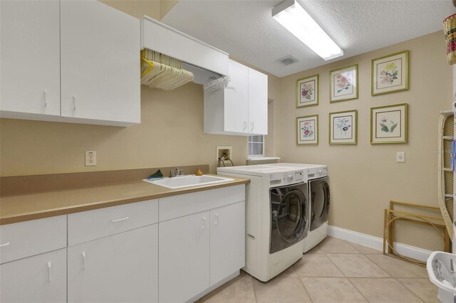 clothes washing area with a textured ceiling, light tile patterned flooring, a sink, cabinet space, and washing machine and clothes dryer