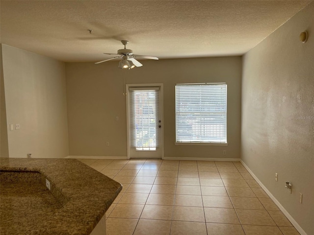 doorway featuring light tile patterned floors, baseboards, a textured ceiling, and a ceiling fan