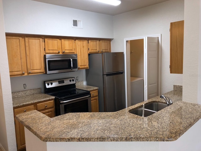 kitchen with visible vents, light stone countertops, a peninsula, stainless steel appliances, and a sink